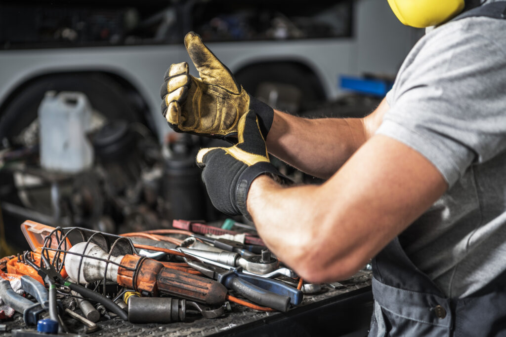Technician in protective gear gives a thumbs-up beside a tool-filled workbench, representing mobile service on heavy equipment.
