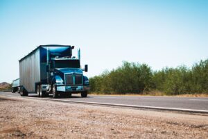 A semi truck driving on a rural highway under blue skies.