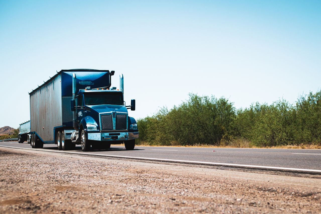 A semi truck driving on a rural highway under blue skies.