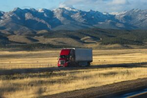 Red semi truck driving on a highway near the mountains.